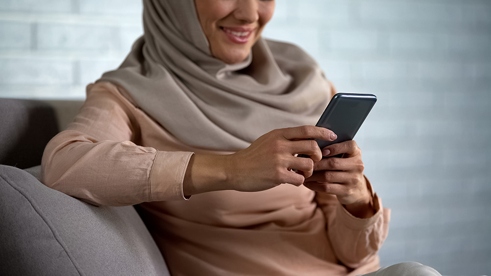 Woman with a grey head scarf seated reading her mobile phone