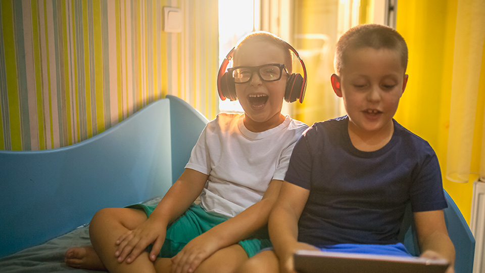 Two children listening to music and reading on an iPad