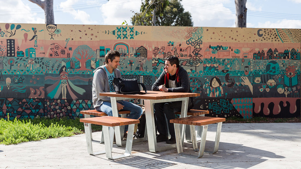 Two people sitting at a table in front of a colorful mural