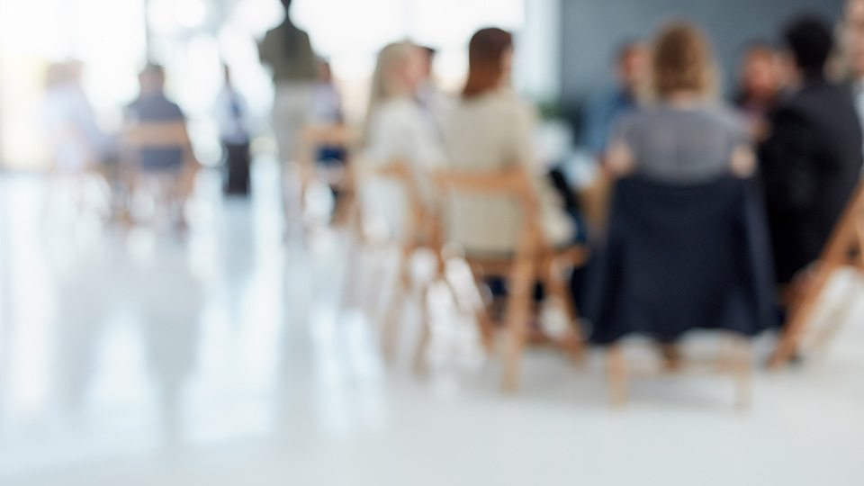 Blurred image of people sitting around a table in a white room