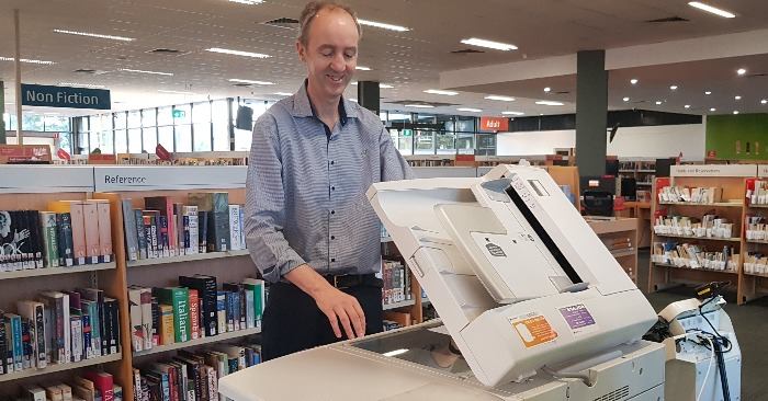 A man scanning papers at a printer in a library