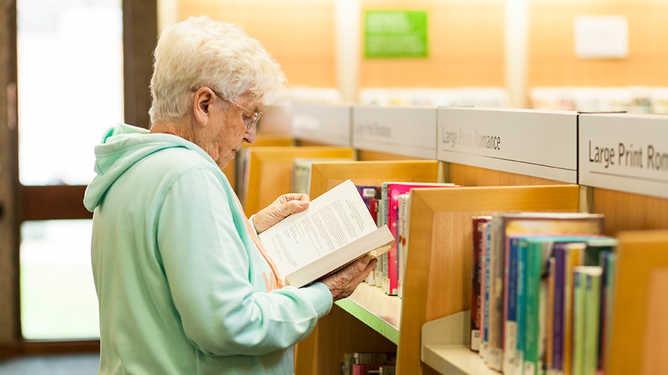An aged woman reading a book at the library