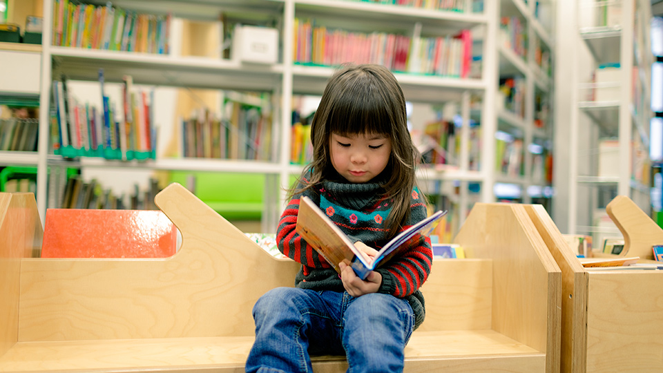 A small child reading a book at a library
