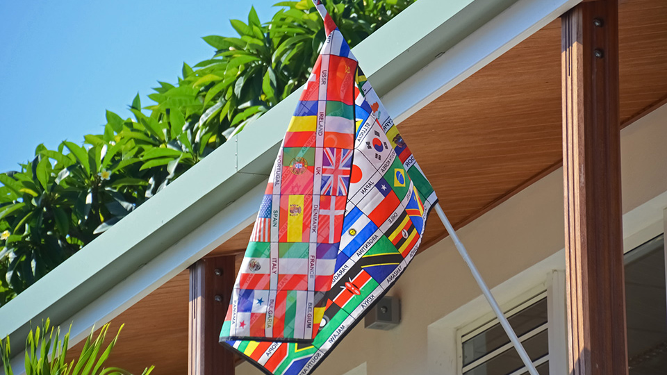 A small outdoor flag hanging at an angle, displaying a collage of smaller international flags.