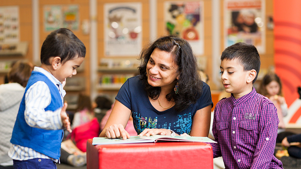 A woman reading to two children in a library setting