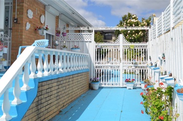 Margaret's Driveway is decorated with blue driveway and white fence. There are hanging pot plants painted blue and white