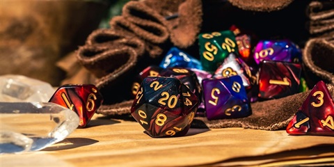 Coloured dice with different numbers of sides spill from a piece of fabric. Two crystals are visible.