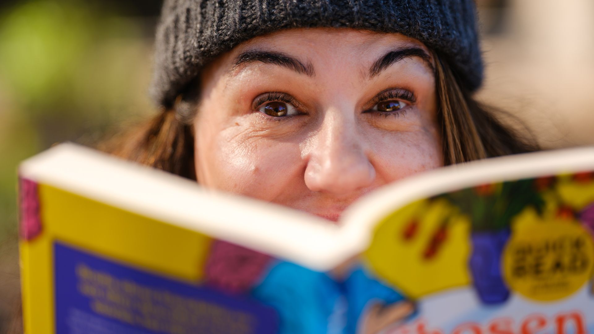 A person holding a book that is covering half of their face.