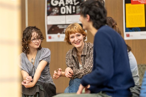 Four young people sitting in a group, smiling and chatting.